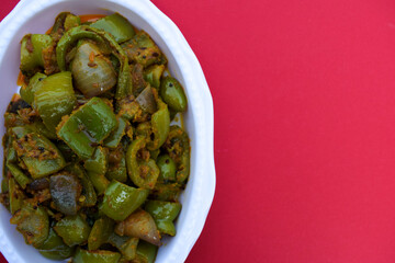 Delicious Capsicum or green bellpepper curry. Stir fried with onions sauted Indian asian sabji with masala. On red background food image copyspace to write text. decorated shimla mirch sabzi