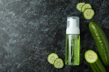 Bottle with cosmetics and cucumber on black smokey background
