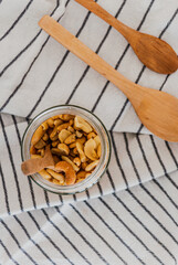 Bodegón de estilo rústico con un bote de vidrio lleno de frutos secos y una cuchara de madera dentro, fuera, dos cucharas de madera de diferentes tamaños sobre una tela de lino blanca con rayas negras