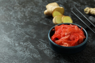 Bowl with red pickled ginger and chopsticks on black smokey background