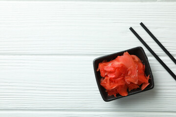 Bowl with red pickled ginger and chopsticks on white wooden background