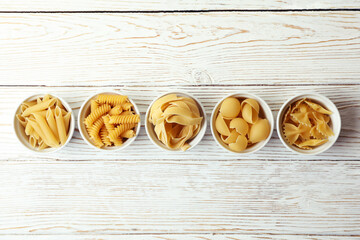 Bowls with uncooked pasta on white wooden background