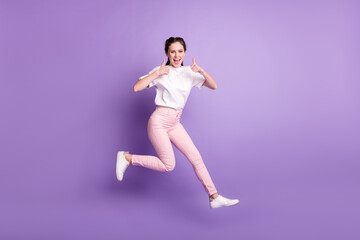 Fototapeta na wymiar Full body photo of happy funky young woman jump up smile make thumbs up isolated on violet color background