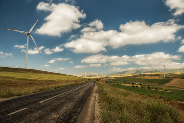 Fototapeta na wymiar Road among hilly terrain with wind turbines and mountains on the horizon.