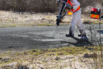 Spring fast repair of an asphalt road. Worker in uniform during fast repair road surface. repair of...