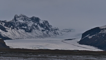 Fototapeta na wymiar Stunning front view of majestic glacier Skaftafellsjökull, part of Vatnajökull ice cap, located in southern Iceland in Skaftafell National Park, surrounded by rugged mountains on cloudy winter day.