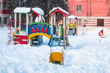 Naklejka premium The playground in the city's residential courtyard is built for the development and entertainment of children. The playground is covered with snow during the winter season.