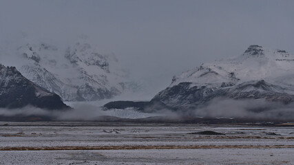 Beautiful view of snow-covered rough mountain range of Öræfajökull in the south of Iceland disappearing in the low clouds with Svínafellsjökull glacier, part of Vatnajökull ice cap, in winter season.