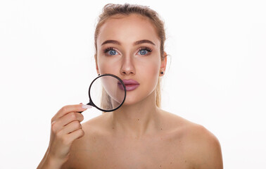 Youth and skin care concept. Beautiful face of young woman with clean fresh skin and blue eyes holds near the face magnifying glass looking at camera isolated on white background with copy space