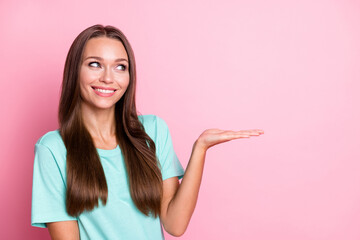 Photo portrait of curious dreamy girl holding empty space on hand smiling isolated on pastel pink...