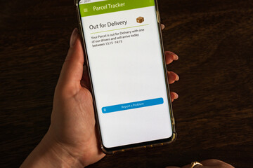 Male thumb finger over parcel delivery app on smartphone screen