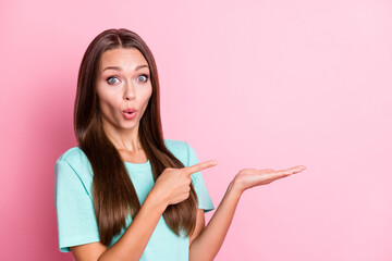 Photo portrait of amazed shocked girl holding blank space on hand pointing finger staring isolated on pastel pink color background
