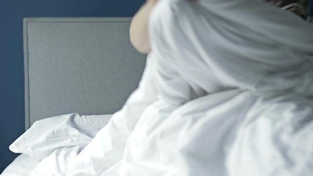 Woman overslept the alarm. She stares in horror at the smartphone screen and jumps out of bed. Early awakening, lack of sleep.