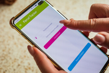 Male thumb finger over parcel delivery app on smartphone screen
