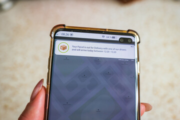 Male thumb finger over parcel delivery app on smartphone screen
