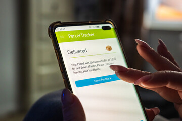 Male thumb finger over parcel delivery app on smartphone screen
