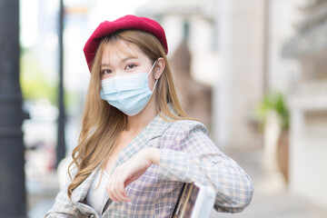 Asian beautiful young woman wears medical face mask in normal lifestyle while sits in park.