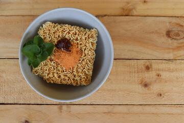 Raw instant noodles with seasonings and vegetables in the bowl, top view isolated on wooden background closeup.
