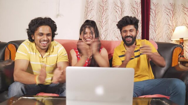 Young siblings enjoying movie on laptop - Friends Clapping for goal or sixer while watching live streaming match from home - concept of sport fans support, enjoyment, technology and internet