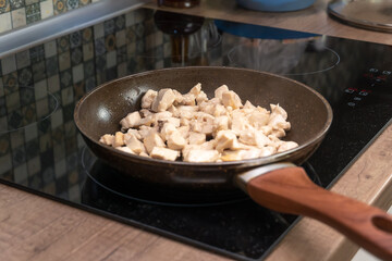 In a frying pan, pieces of chicken meat are fried on an induction stove close-up