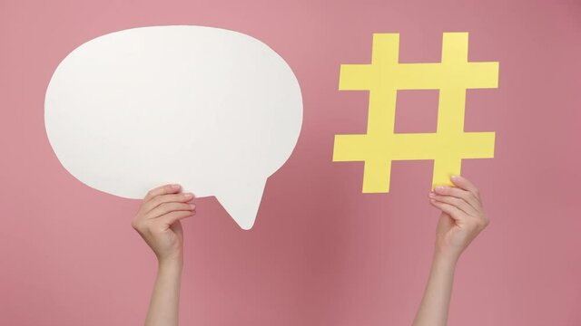 Closeup of hand holding yellow paper hashtag symbol and speech bubble, hash sign of famous media content, isolated on pink background. Post viral web network, blogging blog website strategy concept
