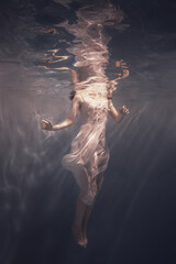 Obraz na płótnie Canvas A girl in a white dress with long dark hair swims underwater as if floating in weightlessness