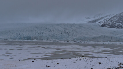 Front view of glacial lake Fjallsárlón in south Iceland with Fjallsjökull glacier, part of the Vatnajökull ice cap, and rugged mountains vanishing in the low clouds in winter.