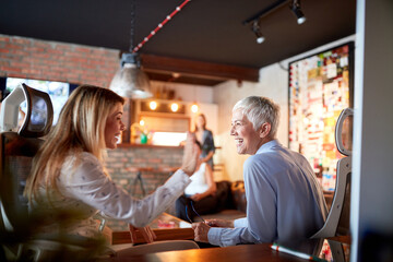 An elderly business woman is having a good time with her young female colleague while they are...