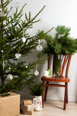 Christmas tree with white toys, old chair with a vase with pine branches, gift boxes under the tree, part of home interior