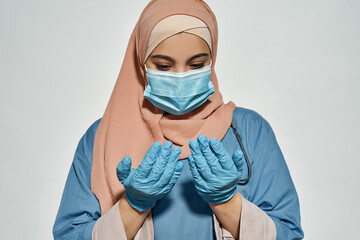 Young arabian girl doctor looking at hands in gloves