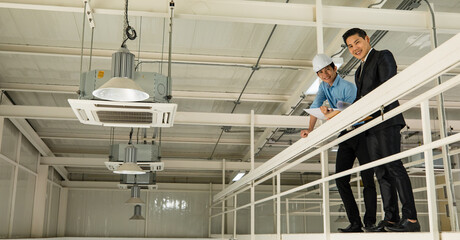Asian businessman boss wearing black suit standing and discussing with young engineer in construction site. Concept for brainstorming, review, and inspecting work results