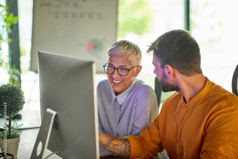 Wall mural an older business woman and a young male colleague talking about a computer screen content they watc