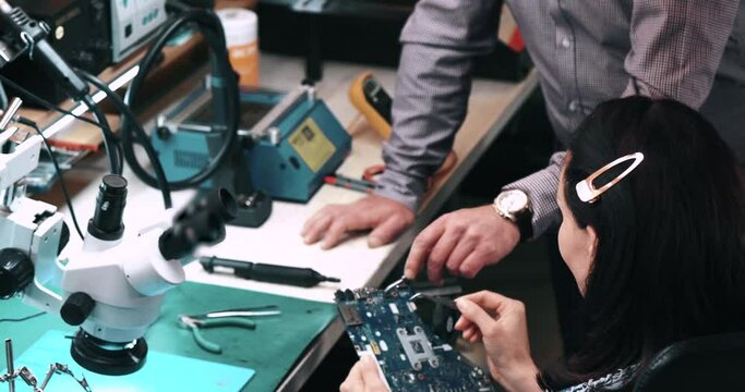 Men and women repair the motherboard using a microscope in the workshop.  Colleagues in computer service