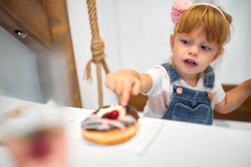 Fototapeta premium A little girl in a pastry shop is amazed by delicious donut. Pastry shop, dessert, sweet