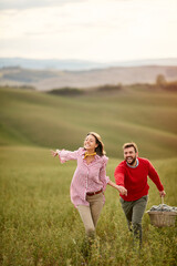 A young cheerful couple running on a large meadow while holding by hands. Love, relationship, together, nature