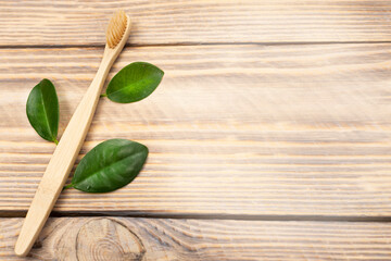 Natural eco friendly bamboo toothbrush with green tree leaves on a wooden background. Choose a wooden toothbrush. Recycling concept, no waste, no plastic, top view
