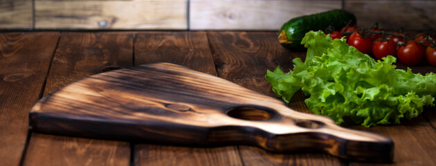 A cutting board in the form of a guitar on a wooden table. Handmade chopping board. Fresh tomatoes, green salad, cucumber and cutting board