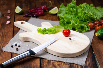 A cutting board in the form of a guitar on a wooden table. Handmade chopping board. Fresh tomatoes, green salad, cucumber and cutting board