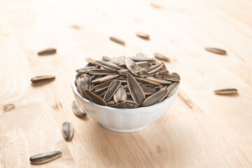 Selective focus pile of sunflower seeds in the white bowl on the wooden table.