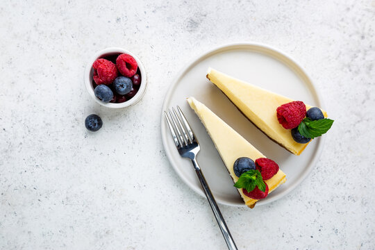 Classic New York cheesecake with fresh berries on white concrete background, top view