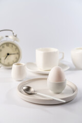 White egg with white plates, cup and alarm clock over white background for breakfast