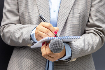 Female journalist at news conference or media event, writing notes, holding microphone