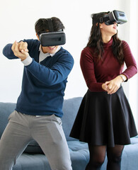 Portrait of cute smiling young Asian lover couple having fun with playing a new video game with virtual reality headset glasses together like fighting or sports game. New digital trending VR concept