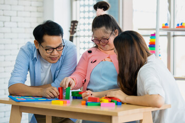 happy Asian family father mother with a handicapped daughter with down syndrome play together.  They are playing with a colorful toy on a wooden table in a living room at home