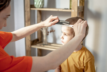 A young woman in bright clothes is cutting a little boy's hair with scissors. Concept of family, care, lifestyle