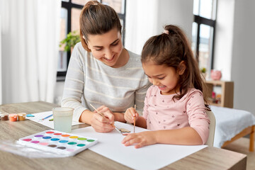 family, motherhood and leisure concept - mother spending time with her little daughter with colors...