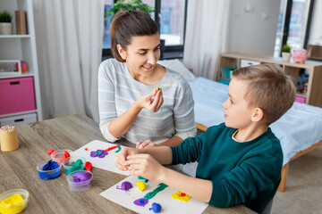 Obraz na płótnie Canvas family, creativity and craft concept - mother and little son making picture of modeling clay at home
