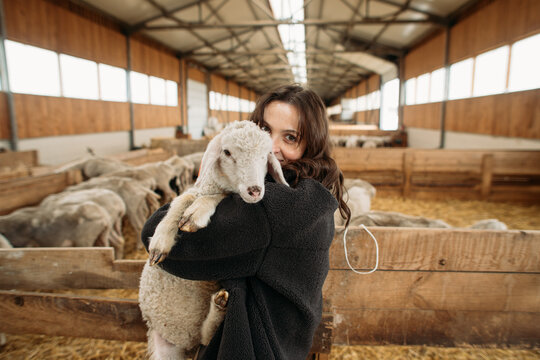 young happy woman on a sheep farm hugging with sheep