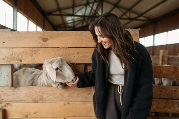 young happy woman on a sheep farm hugging with sheep
