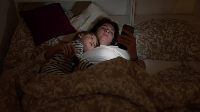 Mother and child lying in bed looking at smartphone at night